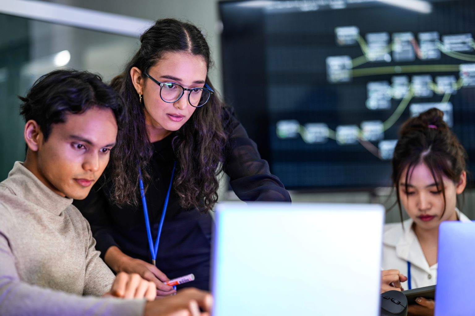 A diverse team of AI developers collaborates on a night coding session. A senior engineer oversees his team, intensely focused on debugging a complex machine learning project.